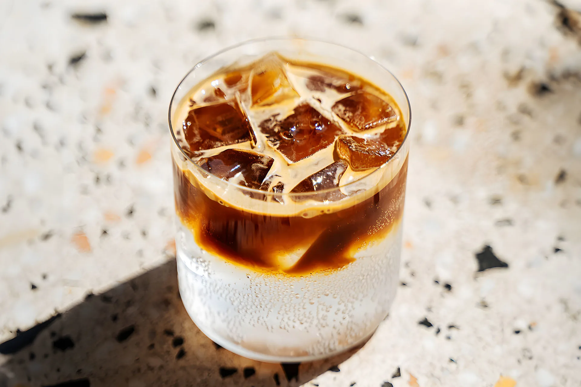 Espresso tonic en vaso alto con hielo y rodajas de naranja sobre mesa de madera