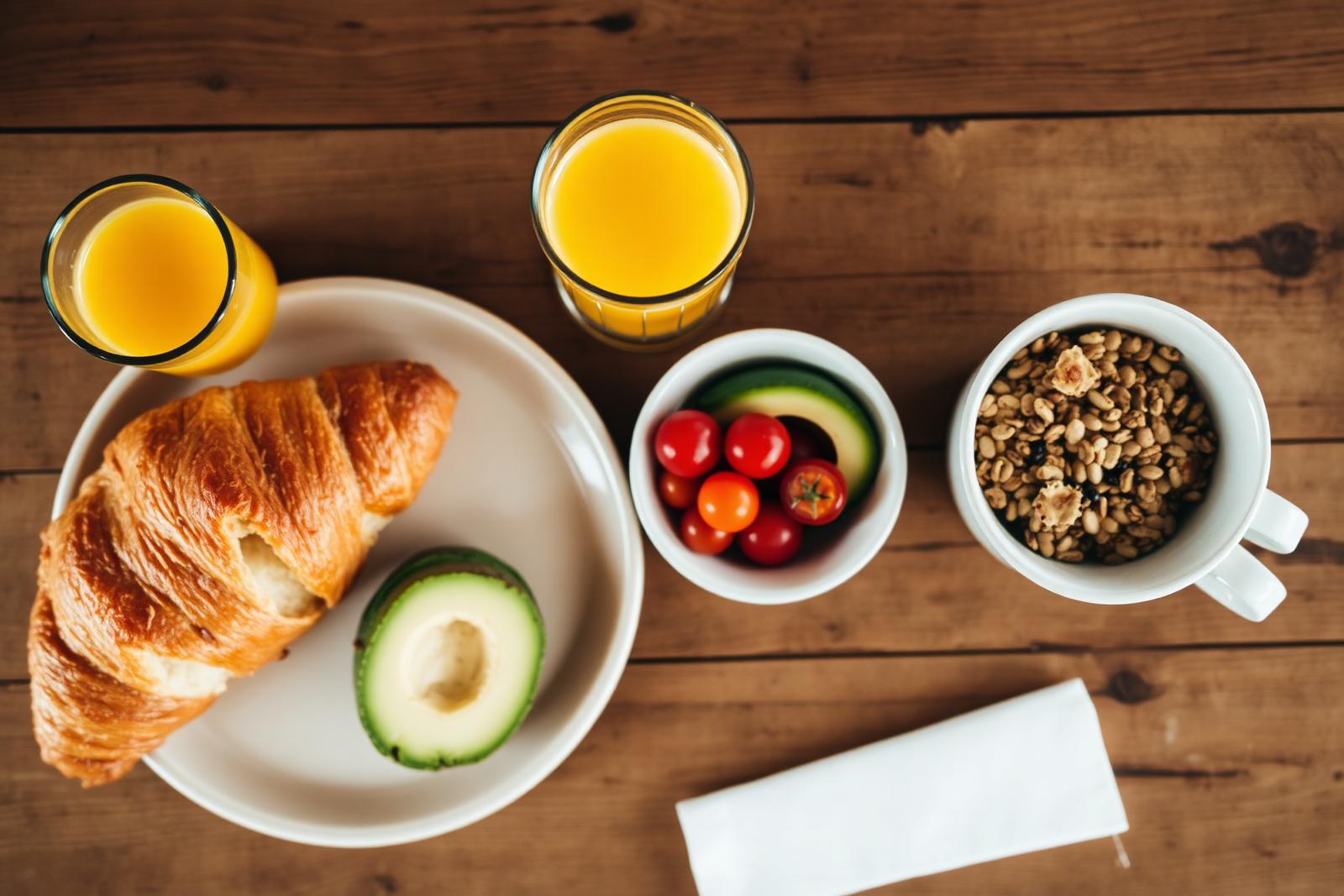 Mesa de madera con croissant, palta, tomates cherry, granola y jugo de naranja en Santos Café & Brunch